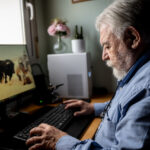 Hombre mayor trabajando en computadora con fondo de ganado