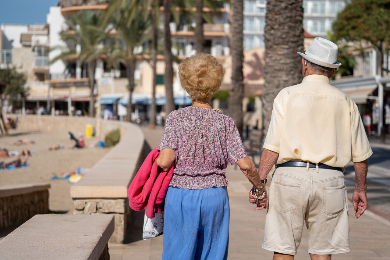 Pareja mayor caminando de la mano por un paseo mar&iacute;timo