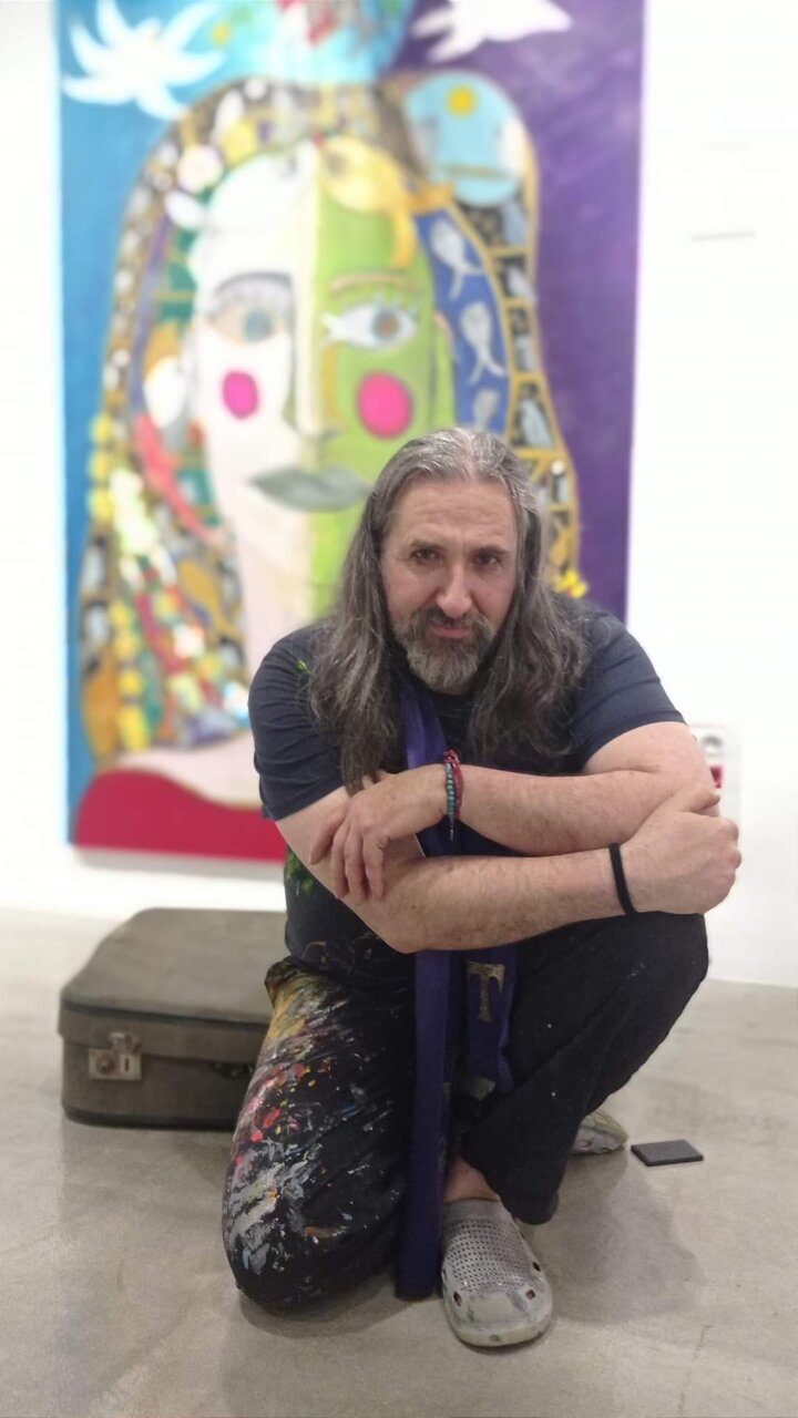Emanuel Navarro D'Garem posando en su estudio art&iacute;stico con una obra colorida detr&aacute;s.