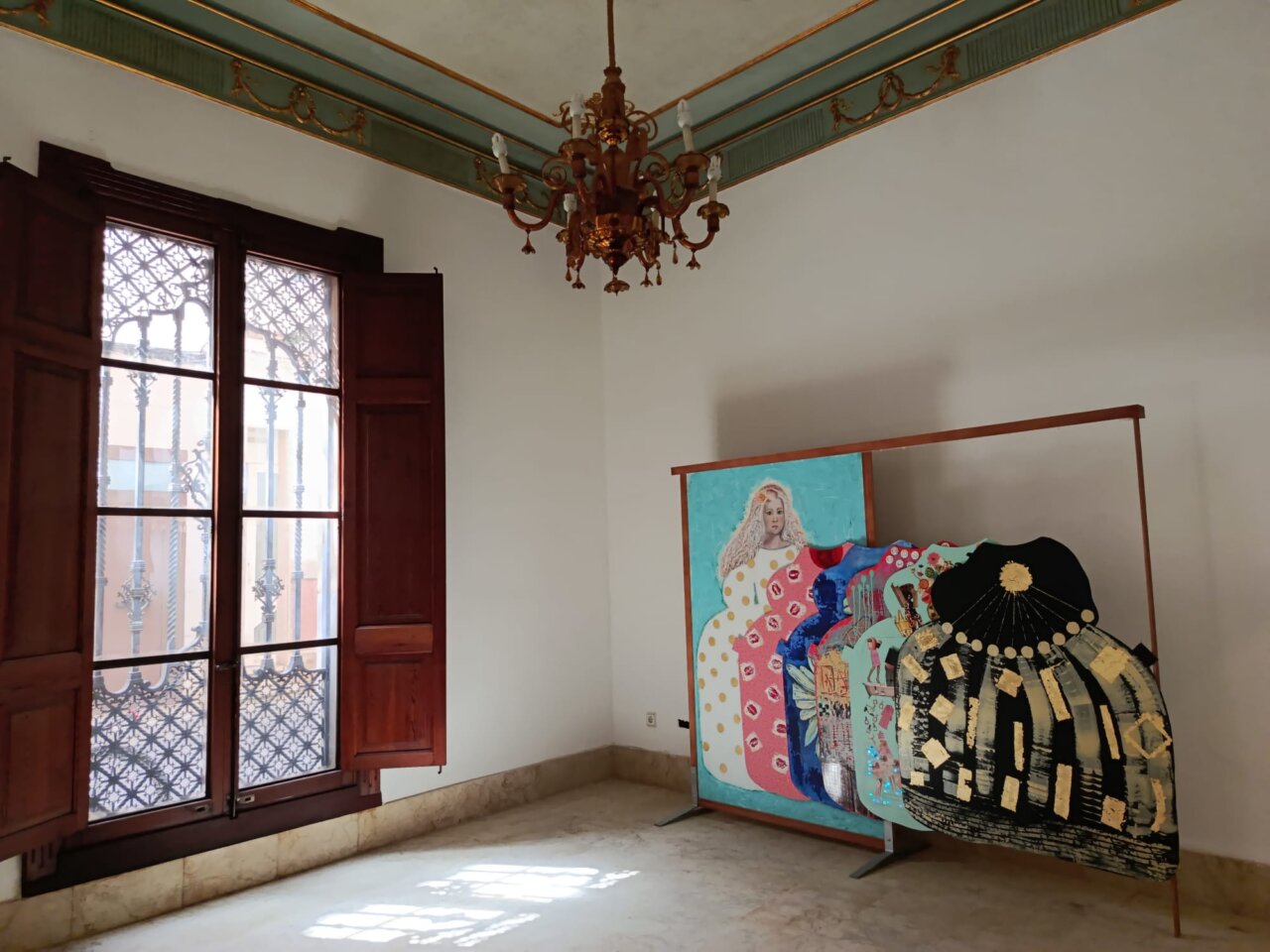 Interior de una habitaci&oacute;n con una obra de arte colorida y ventanas abiertas