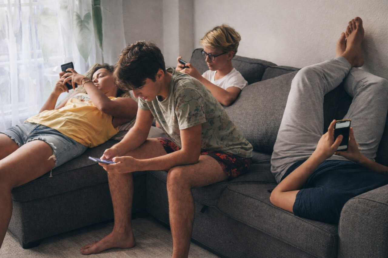 Cuatro adolescentes sentados en un sof&aacute; usando sus tel&eacute;fonos m&oacute;viles.
