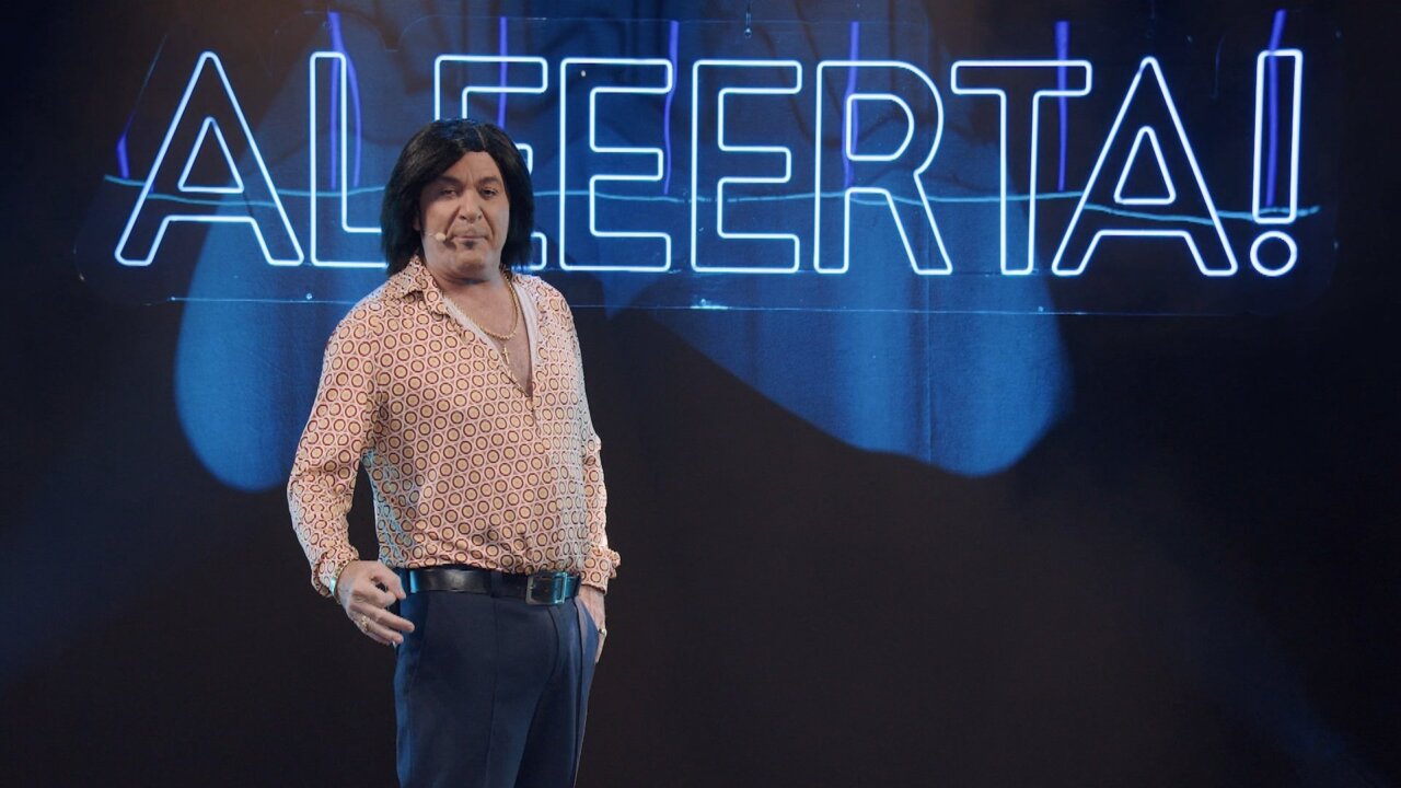Hombre con cabello largo y camisa de estampado en un escenario