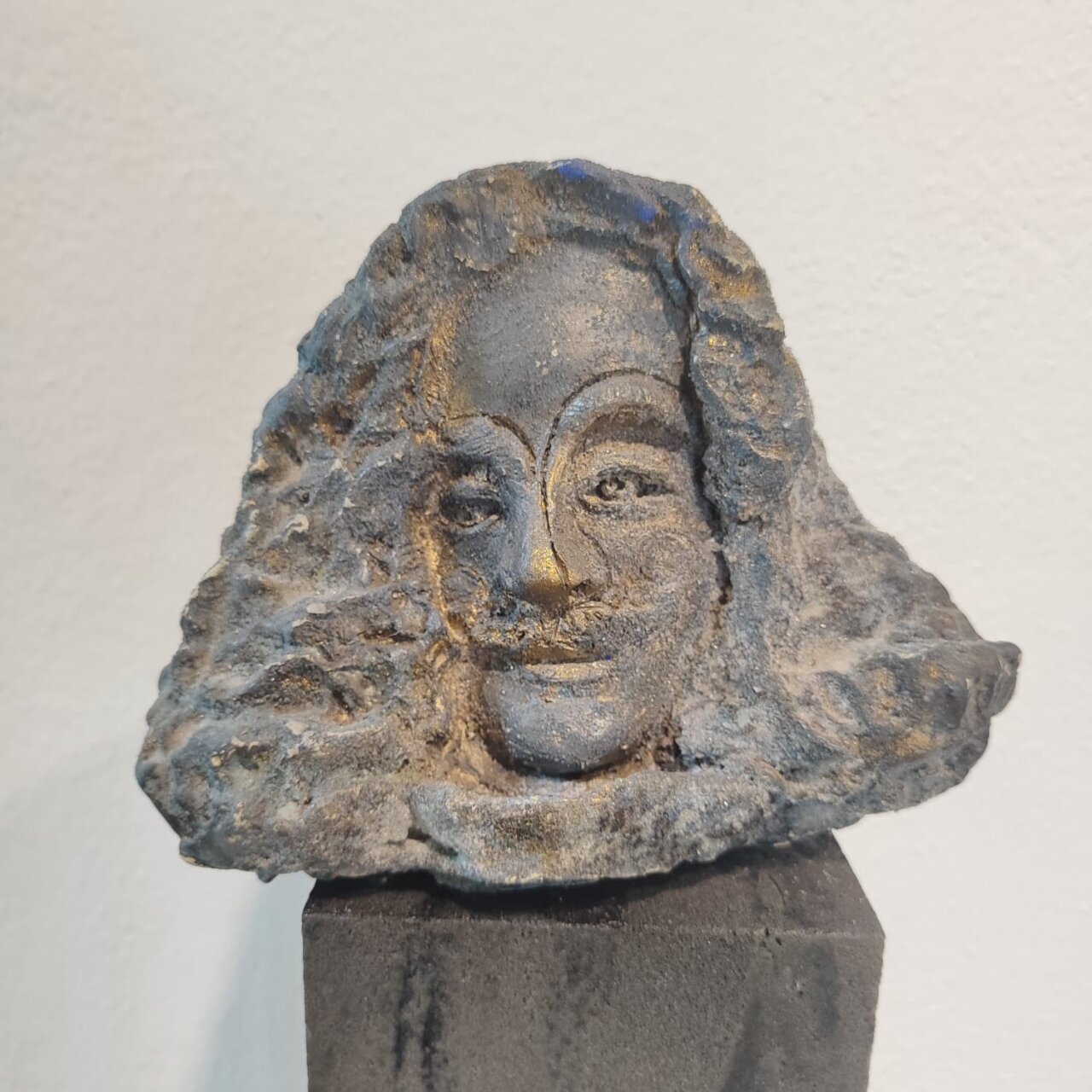 Escultura en relieve de un rostro con cabello rizado y expresi&oacute;n serena