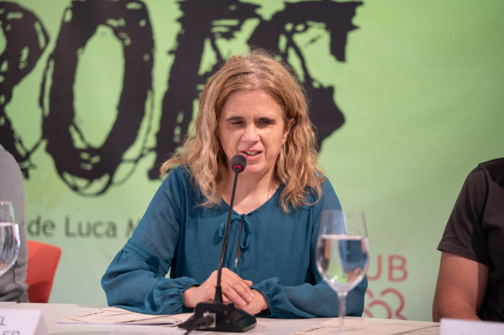 Mujer hablando en un evento con micr&oacute;fono y vaso de agua