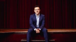 Fernando Miralles sentado en un escenario, vestido de traje azul.