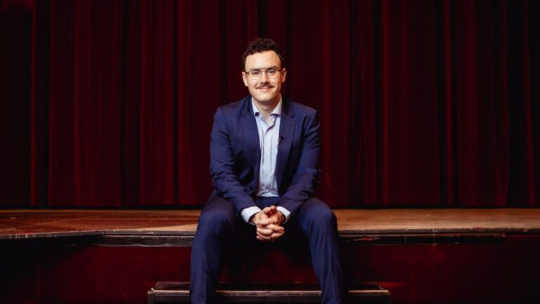 Fernando Miralles sentado en un escenario, vestido de traje azul.