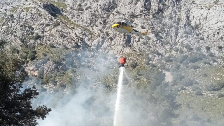 Helic&oacute;ptero apagando un incendio forestal en Escorca con un balde de agua.