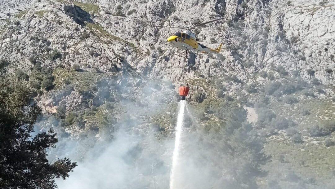 Helic&oacute;ptero apagando un incendio forestal en Escorca con un balde de agua.