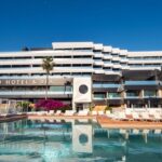 Vista exterior del Hotel El Corso en Ibiza con piscina y palmeras