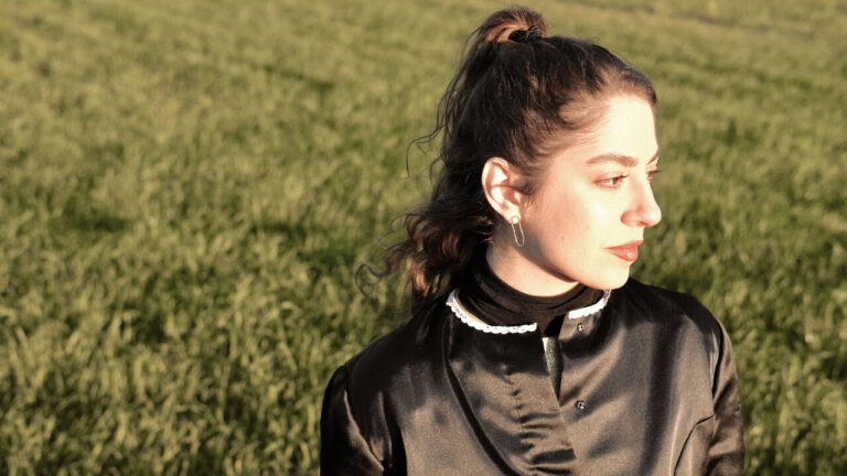 Maria Jaume en un campo verde, luciendo un atuendo elegante y reflexivo.