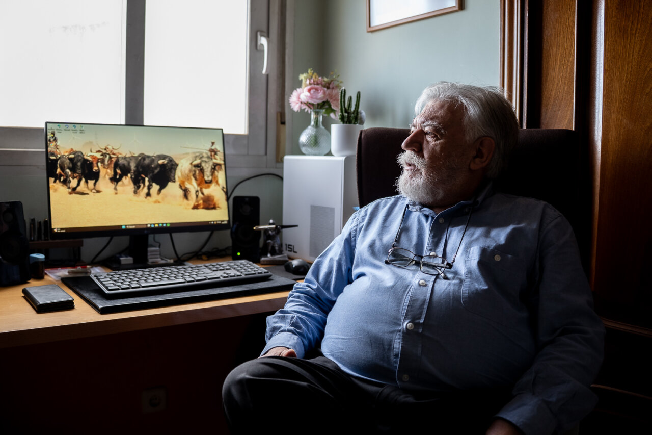 Hombre mayor sentado frente a un ordenador con fondo de ganado