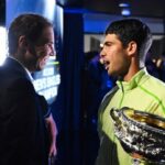 Rafa Nadal sonr&iacute;e mientras felicita a Carlos Alcaraz con el trofeo.