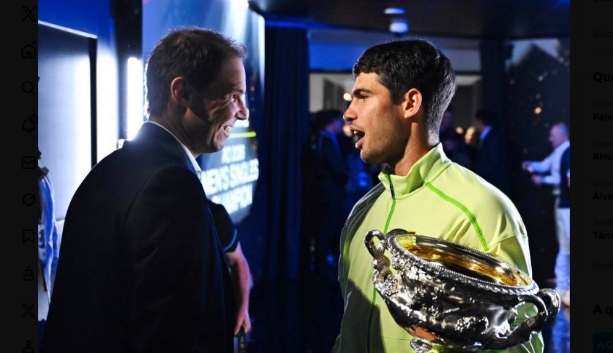 Rafa Nadal sonr&iacute;e mientras felicita a Carlos Alcaraz con el trofeo.