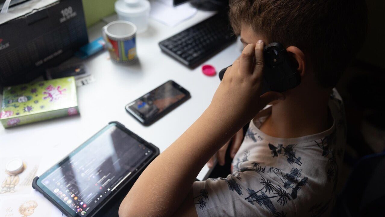 Ni&ntilde;o usando una tablet mientras sostiene un tel&eacute;fono m&oacute;vil