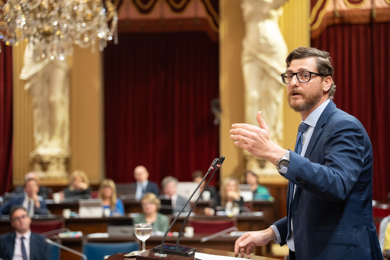 Hombre hablando en el Parlamento con p&uacute;blico atento detr&aacute;s