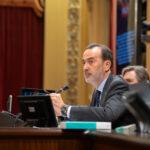 Hombre en traje hablando en el Parlamento con micr&oacute;fono y pantallas