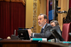 Hombre en traje hablando en el Parlamento con micr&oacute;fono y pantallas