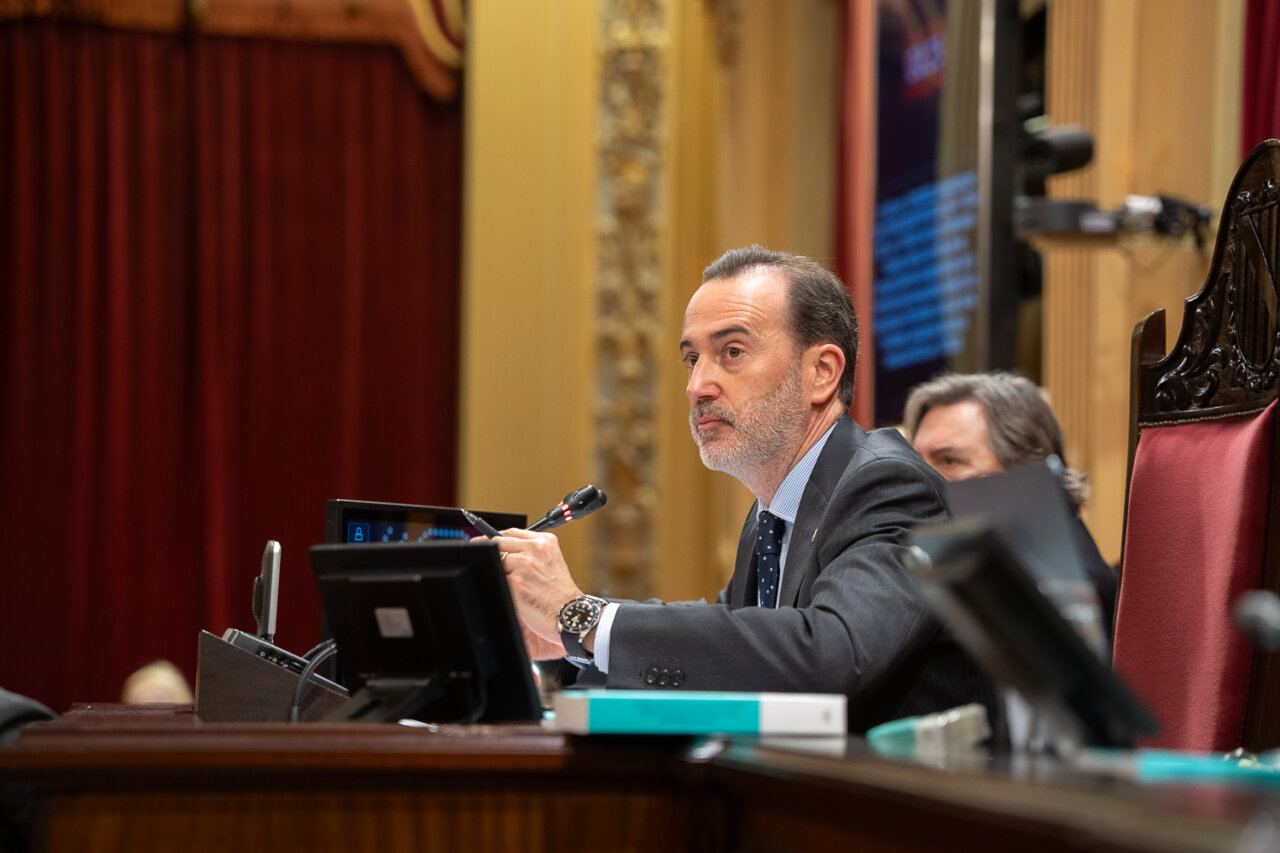 Hombre en traje hablando en el Parlamento con micr&oacute;fono y pantallas