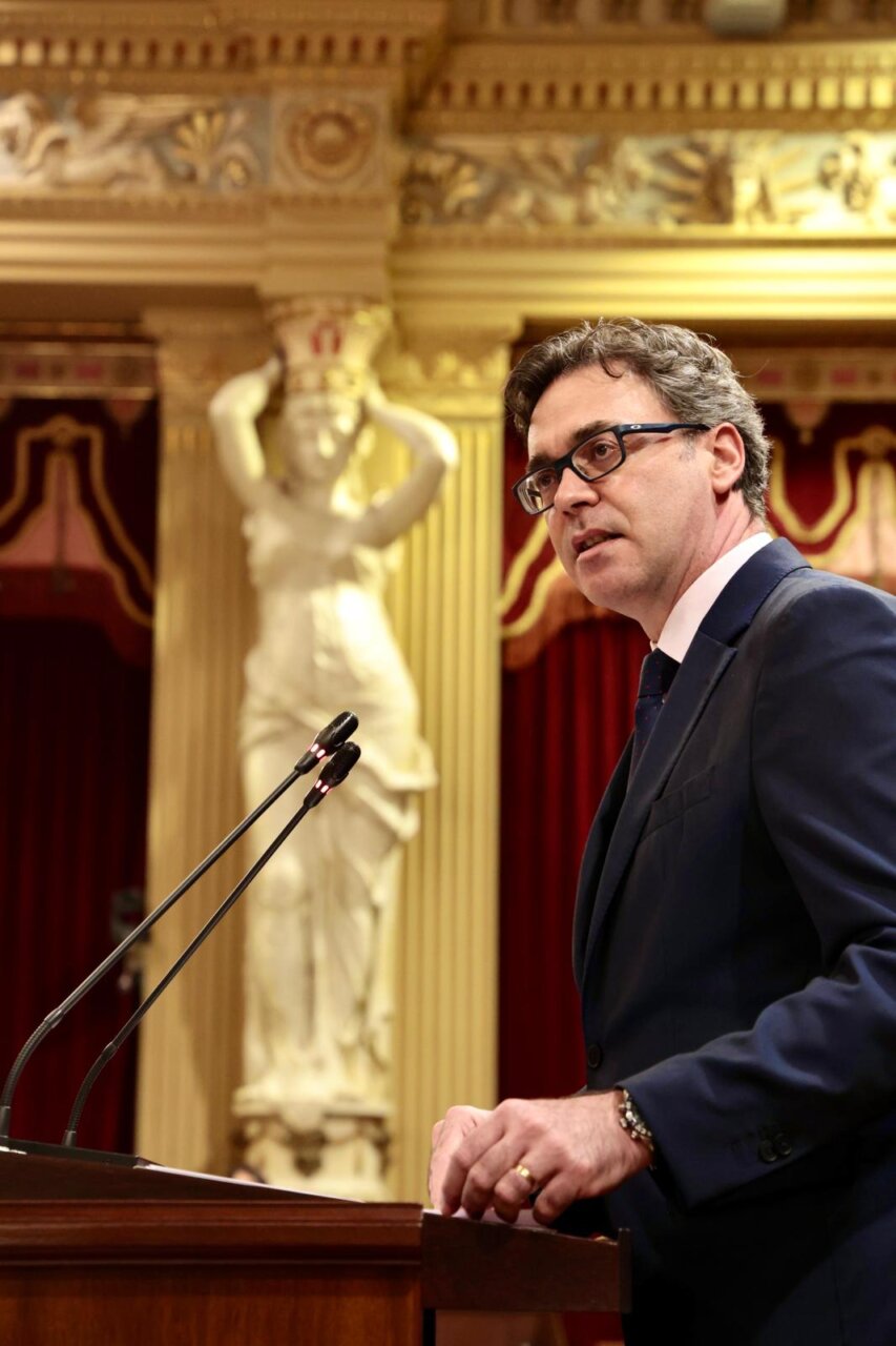 Hombre hablando en un podio en un entorno formal con decoraci&oacute;n cl&aacute;sica