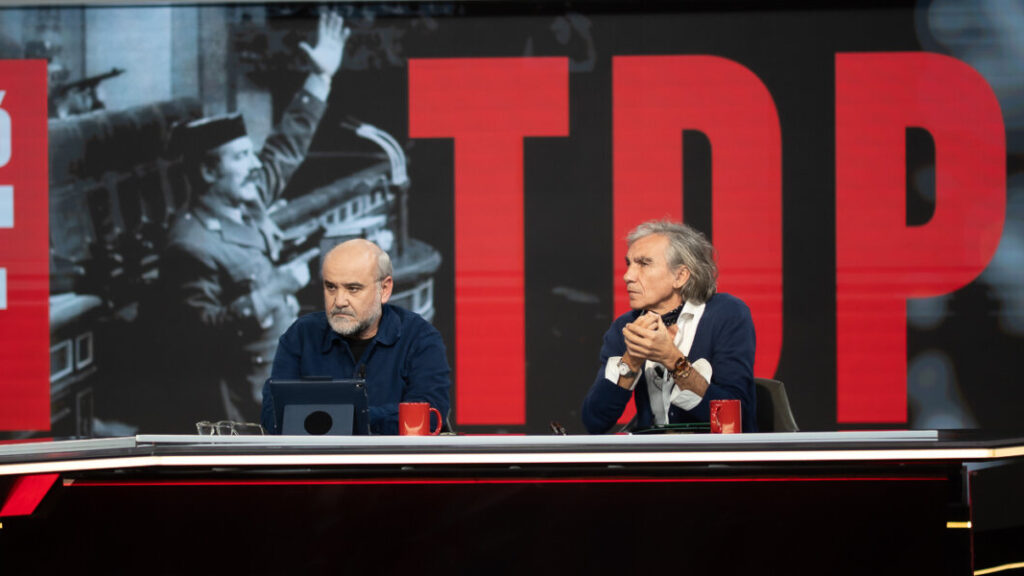 Dos presentadores en un set de televisión discutiendo un tema importante.