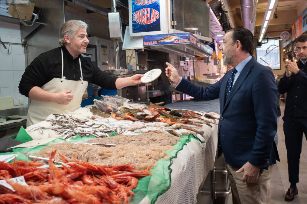 Hombre en un mercado de pescado interactuando con un cliente.
