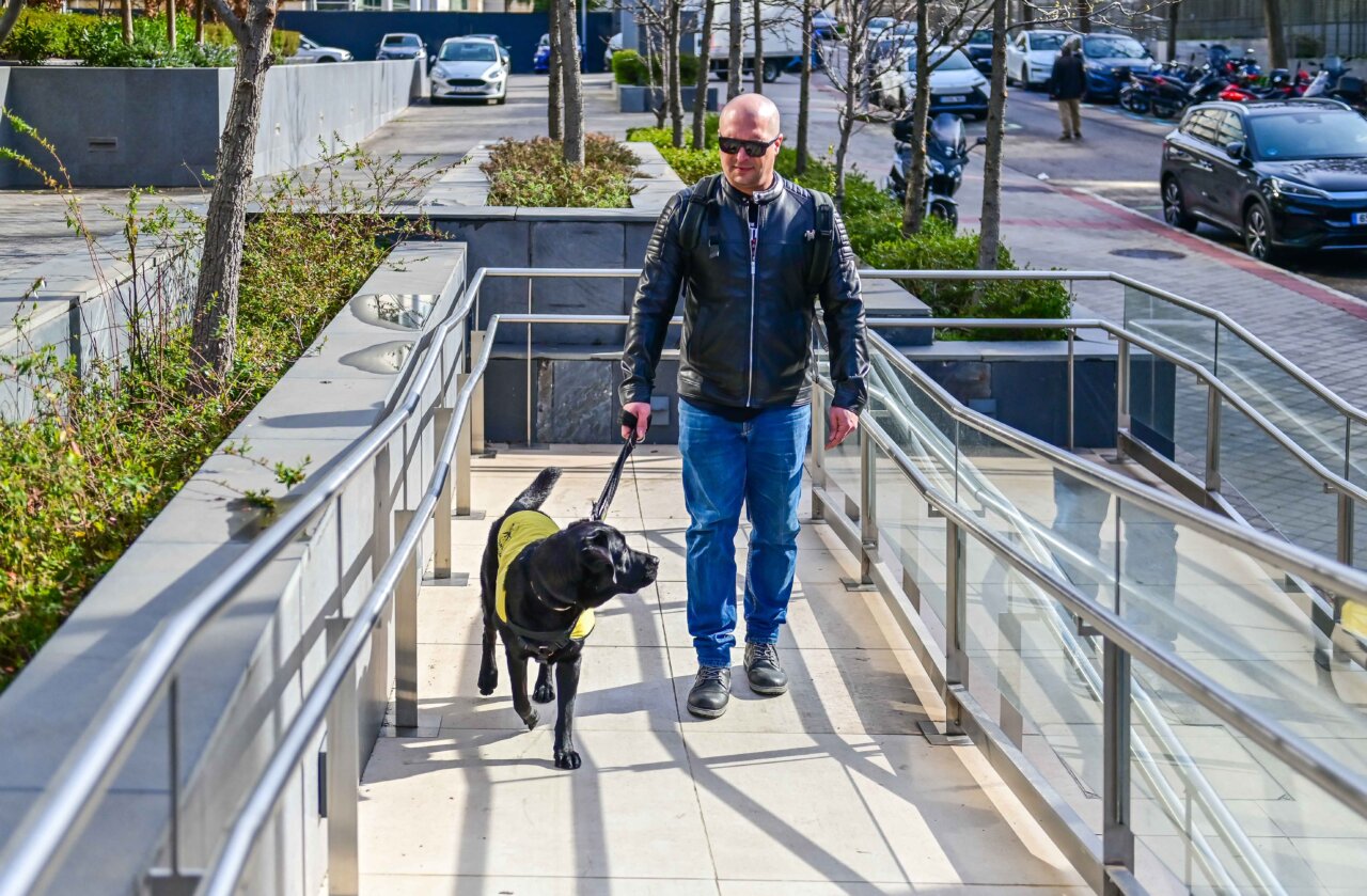 Hombre con gafas de sol y perro gu&iacute;a en rampa accesible