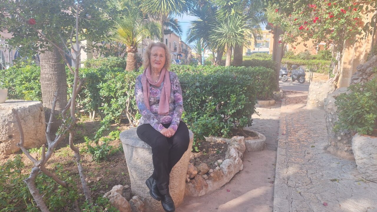 Marita Torres sentada en un parque rodeada de plantas y flores