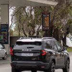 Gasolinera con precios de gasolina visibles y coches en la calle