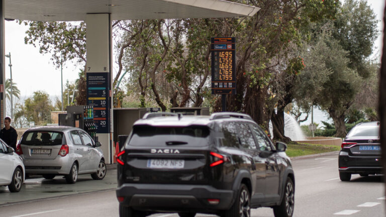 Gasolinera con precios de gasolina visibles y coches en la calle