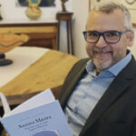 Hombre sonriendo sosteniendo un libro sobre Antoni Maura en una mesa