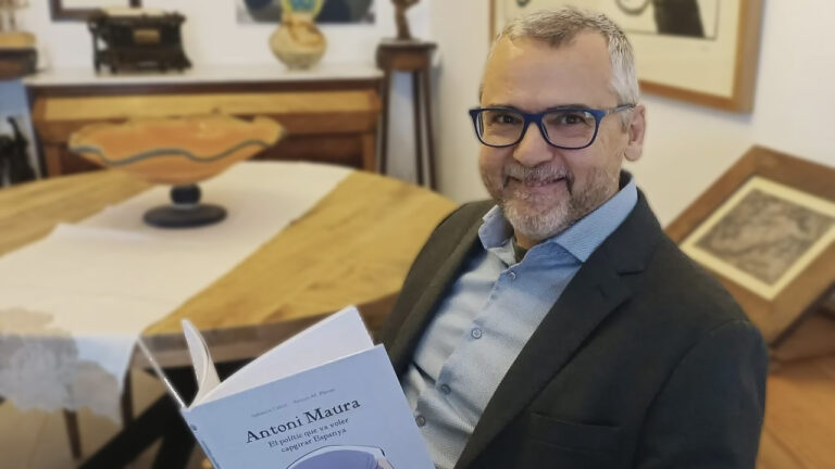 Hombre sonriendo sosteniendo un libro sobre Antoni Maura en una mesa