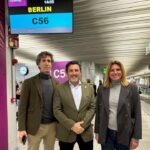 Tres personas en un aeropuerto con un cartel de vuelo a Berlín