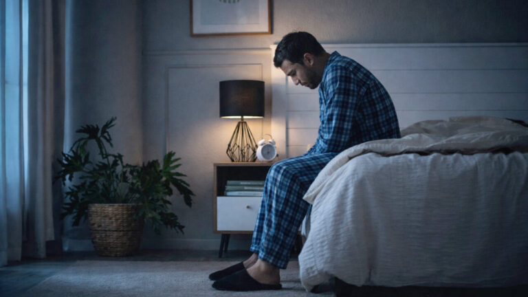 Hombre sentado en la cama con pijama, mirando hacia abajo