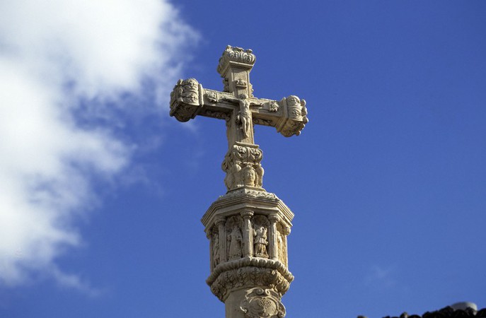 Cruz de piedra decorada con figuras en un cielo azul despejado