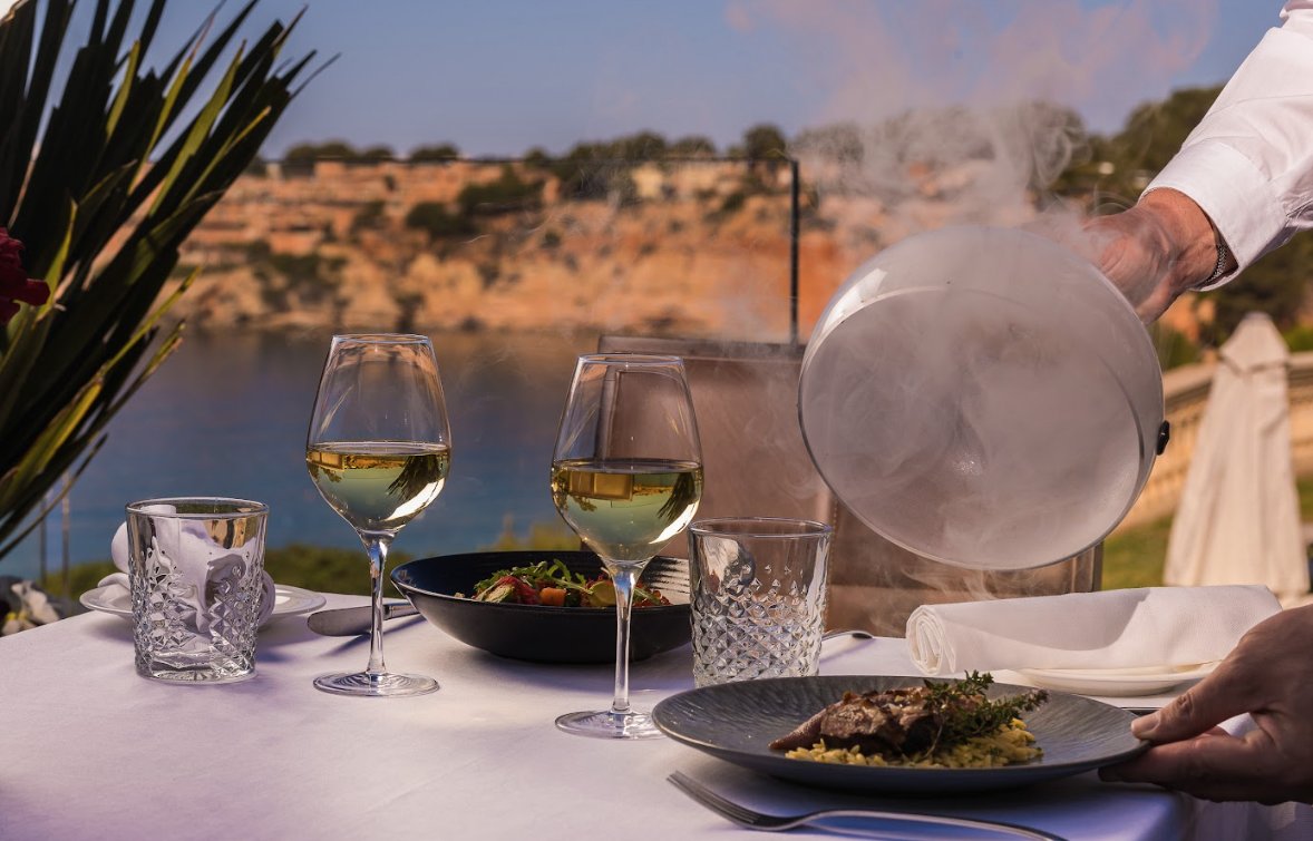 Mesa con platos gourmet y copas de vino en un restaurante frente al mar