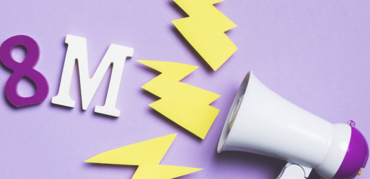Meg&aacute;fono y letras 8M sobre fondo morado, simbolizando la lucha por la igualdad de g&eacute;nero.