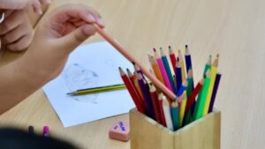 Mano de ni&ntilde;o sosteniendo un l&aacute;piz junto a un vaso de colores