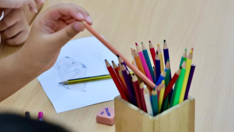 Mano de niño sosteniendo un lápiz junto a un vaso de colores