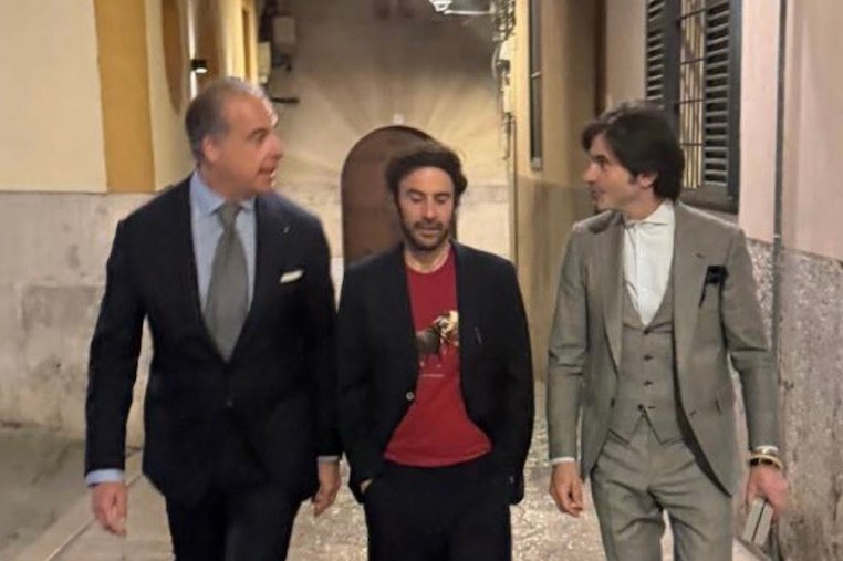 Tres hombres conversando en una calle, vestidos elegantemente.