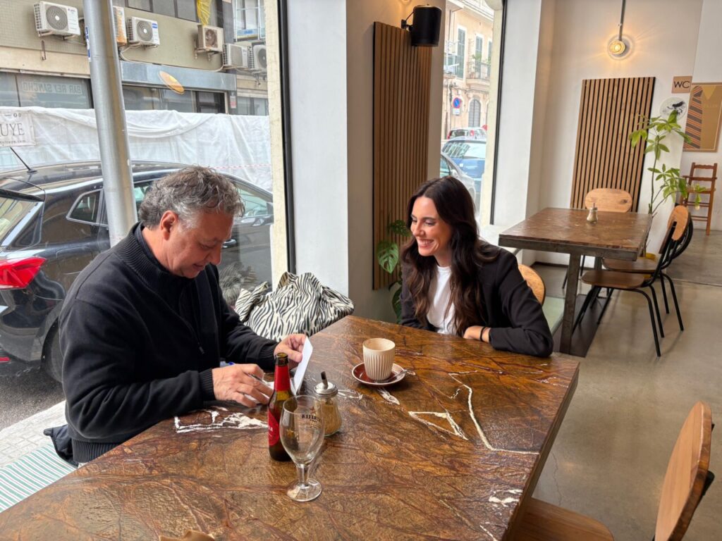 Magda Trobat conversando en un bar con un hombre mientras sonr&iacute;e.