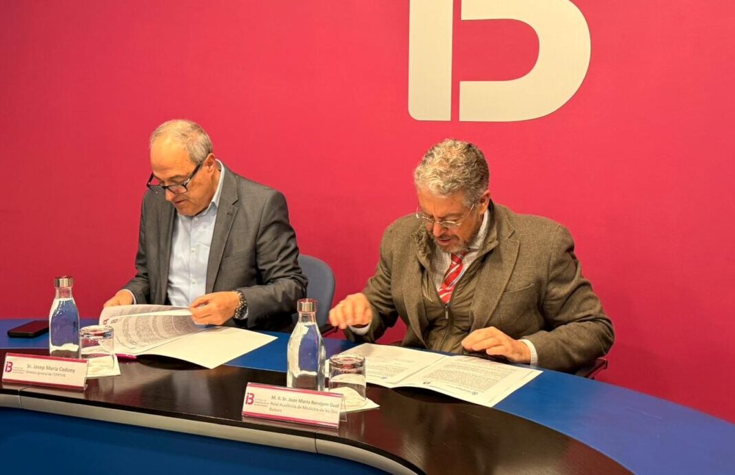 Dos hombres firmando un convenio en una mesa con documentos.