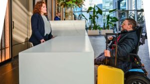 Recepci&oacute;n de hotel con una mujer y un hombre en silla de ruedas.