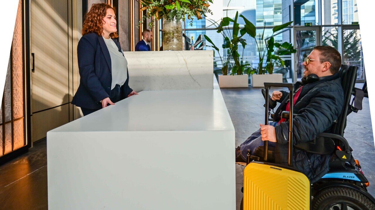 Recepci&oacute;n de hotel con una mujer y un hombre en silla de ruedas.