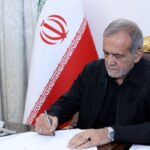 Masud Pezeshkian firmando documentos en su oficina con la bandera de Ir&aacute;n de fondo