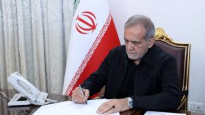 Masud Pezeshkian firmando documentos en su oficina con la bandera de Ir&aacute;n de fondo