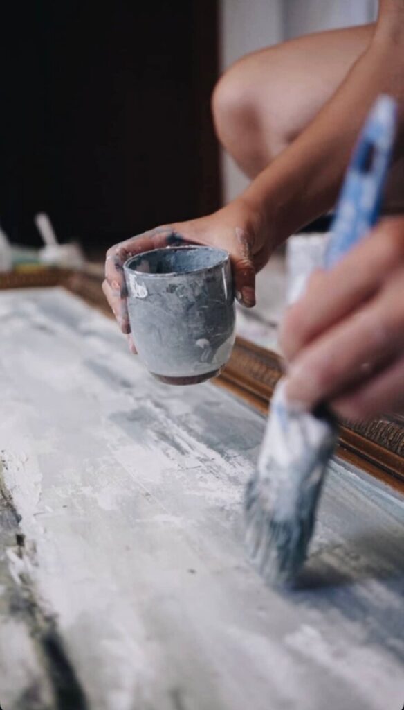 Mano sosteniendo un vaso y brocha en proceso de pintura