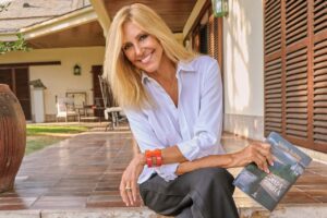 Marta Robles sonriente sosteniendo su novela Amada Carlota en un entorno acogedor.