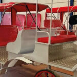 Calesa el&eacute;ctrica con asientos rojos y estructura blanca en un taller