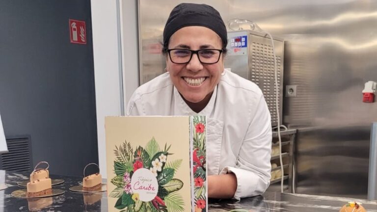 Chef sonriente sosteniendo un men&uacute; en una cocina moderna