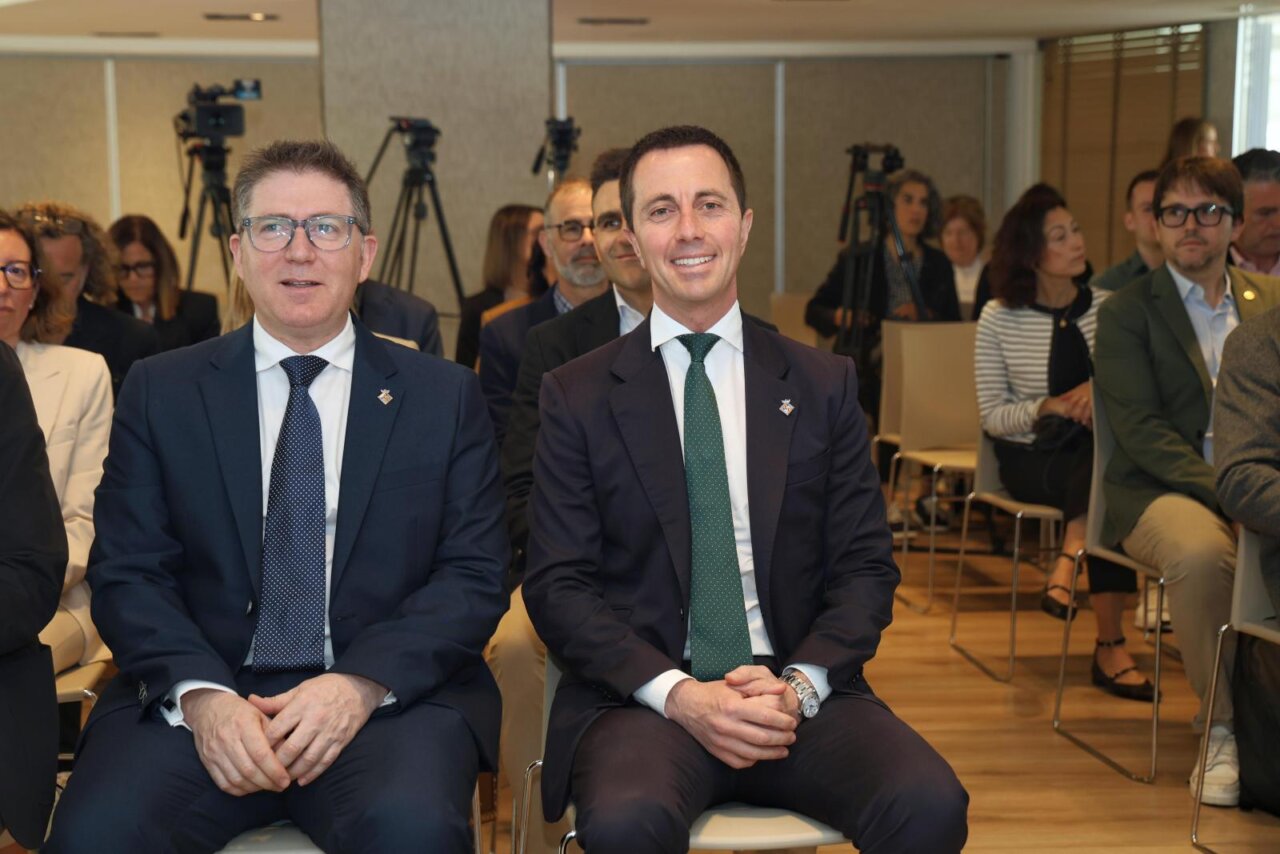 Dos hombres sentados en un evento en Mallorca, con p&uacute;blico al fondo.